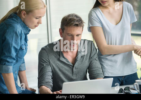 Workers gathered around desk of colleague Stock Photo