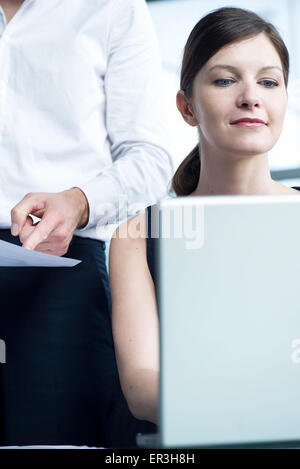 Woman working on laptop computer, boss watching over her shoulder Stock Photo
