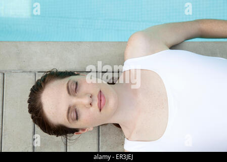 Young woman sunbathing by pool with eyes closed, overhead view Stock Photo