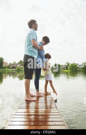 Family with young daughter standing together at end of lake pier Stock Photo