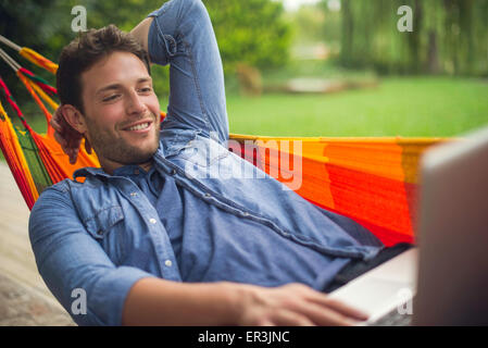 Man reclining in hammock using laptop computer Stock Photo