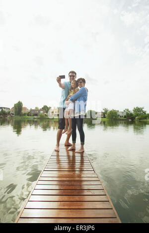 Family with young daughter standing together at end of lake pier taking selfie Stock Photo