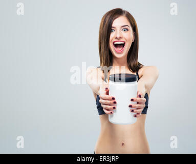 Cheerful smiling sporty woman with jar of protein over gray background and looking at camera Stock Photo