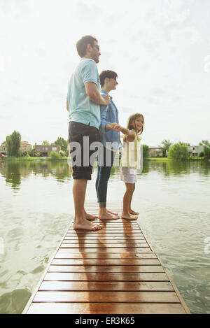 Family with young daughter standing together at end of lake pier Stock Photo