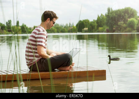 Man sitting on dock using laptop computer Stock Photo