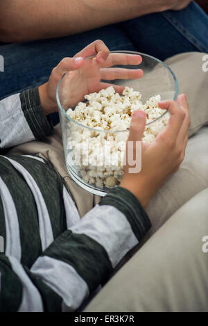 Child holding bowl of popcorn on lap, cropped Stock Photo