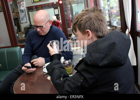 Father and son checking mobile phones in café. Stock Photo