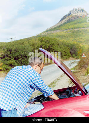 Adult man is standing near his broken car waiting for tow Stock Photo