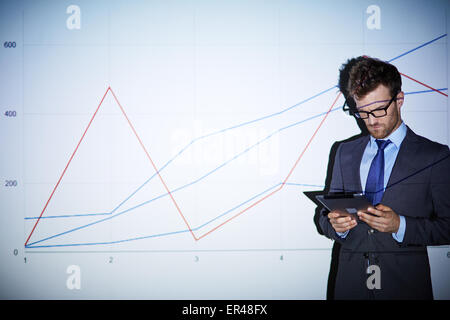 Serious businessman with touchpad standing by wall with graph Stock Photo