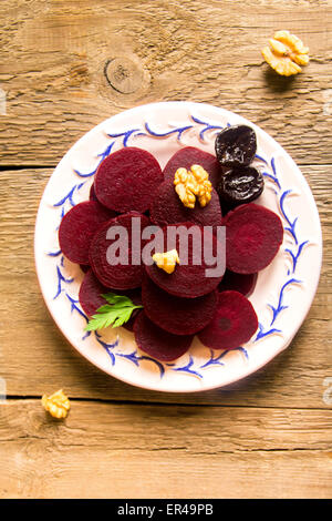 Boiled sliced beetroots on plate with walnuts and parsley over rustic wooden table. Ingredient of traditional russian cuisine. Stock Photo