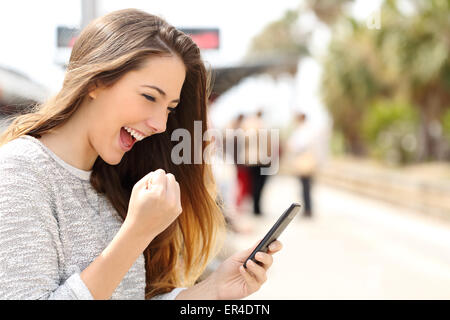 Euphoric woman watching her smart phone in a train station while is waiting Stock Photo