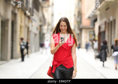 Front view of a fashion happy woman walking and using a smart phone on a city street Stock Photo
