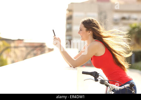 Profile of a teen girl using a mobile phone in a park in a sunny summer day with the wind moving her hair Stock Photo