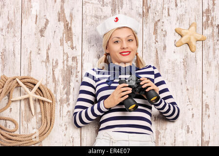 Female sailor lying on a deck with binoculars in her hand and looking at the camera Stock Photo