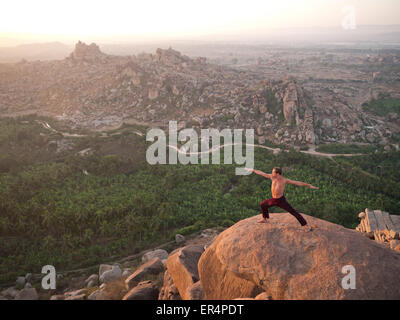 A man in yoga warrior pose in Hampi at sunrise India Stock Photo