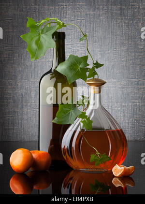 Still life composition with bottles leafs and mandarins on dark background Stock Photo