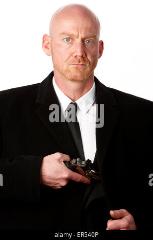 bald headed man wearing heavy black overcoat showing revolver in inside pocket against a white studio background model released Stock Photo