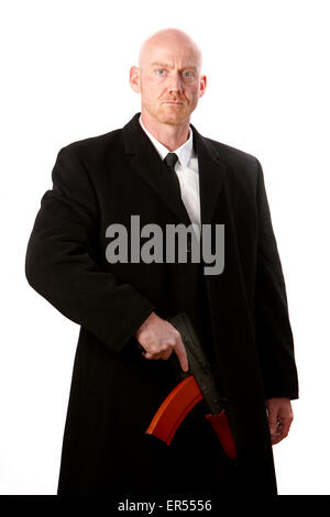 bald headed man wearing heavy black overcoat holding ak-47 against a white studio background model released image Stock Photo