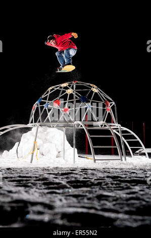 A snowboarder  jumps over a jungle gym at night in Saint Paul, Minnesota.