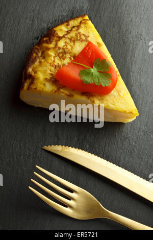 Spanish omelette on black plate with golden fork and knife Stock Photo