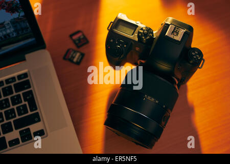Still life of dslr camera, sdhc flash memories and laptop computer on wooden table. High angle view of objects with sunset light Stock Photo