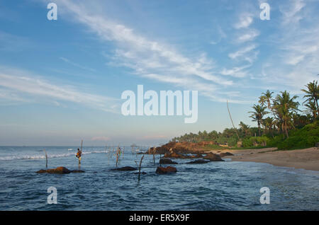 Stilt fishermen in the early morning in front of a rocky coastline near Weligama, South Sri Lanka Stock Photo