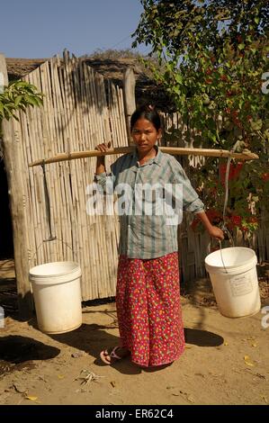 Burmese woman wearing a Longyi skirt, carrying water with a wooden pole and two buckets, Bagan, central Myanmar, Myanmar Stock Photo