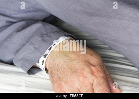 Close up of the arm of a middle aged  man in grey pyjamas in bed with a hospital patient ID wristband visible on left wrist. Stock Photo
