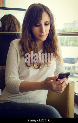Young cheerful woman sitting in restaurant using smartphone. Warm color toned image of pretty girl with gadget in cafe