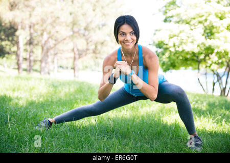 Smiling sporty woman doing stretching exercise outdoors in park. Looking away Stock Photo