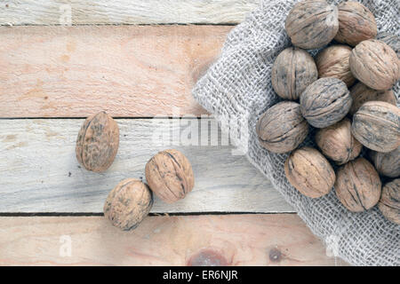 Some walnuts scattered on a table and a sack in a rustic wooden kitchen, top view Stock Photo