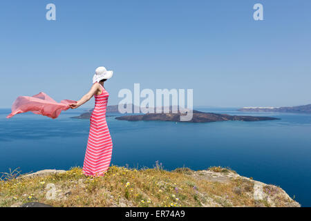 Woman in a long summer dress standing in a field of daisies, on the beach sea. Greece, Santorini Stock Photo