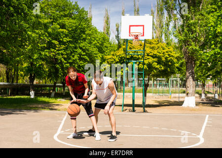 Young Athletic Couple Playing Basketball Together on Outdoor Court in Lush Green Park Stock Photo