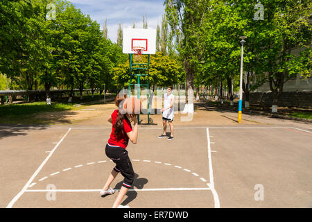 Young Athletic Couple Playing Basketball Together - Man Watching as Woman Takes Shot from Top of Key on Outdoor Court in Lush Gr Stock Photo