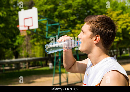 Head and Shoulders View of Young Man Drinking Water from Bottle, Taking a Break for Refreshment and Hydration on Basketball Cour Stock Photo
