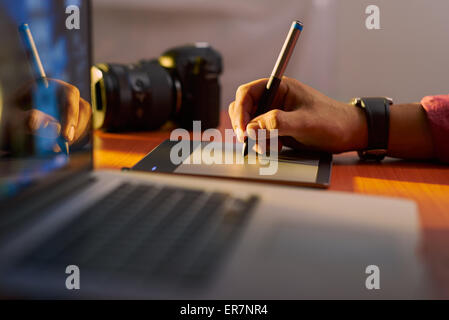 Photographer drawing and retouching image on laptop computer, using a digital tablet and stylus pen. Closeup of man's hand Stock Photo
