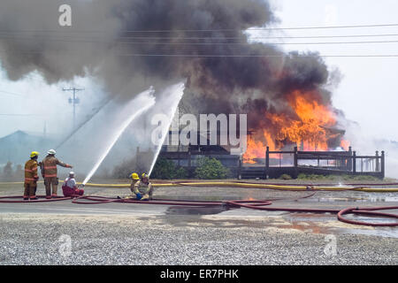 Firemen spray water on an abandoned building that has be set afire for firefighter training purposes on Cape Hatteras in North Carolina, USA. Stock Photo