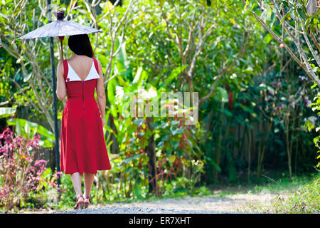 Beautiful woman in red dress walking through a Thai garden