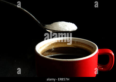 A spoonful of sugar is poured into a cup of coffee Stock Photo