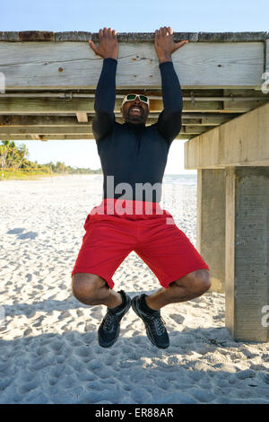 Man doing pull ups on a beach pier Stock Photo