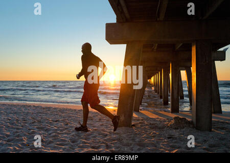 Man running under a pier on the beach at sunset Stock Photo