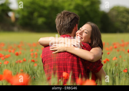 Happy couple hugging affectionate after proposal in a green field with red flowers Stock Photo