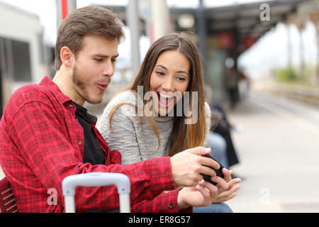 Funny couple playing games with a smart phone in a train station while they are waiting Stock Photo