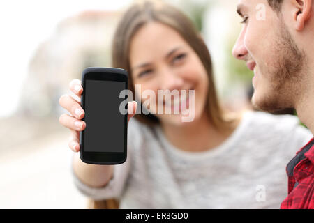Happy couple showing apps in a blank smart phone screen outdoors Stock Photo
