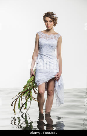 Portrait of young bride holding dress and wilted bouquet while standing in water against white backg Stock Photo