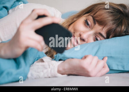 Young woman using mobile phone while relaxing in bed Stock Photo