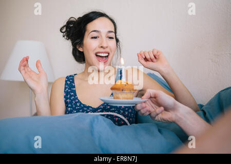 Surprised young woman blowing out candle on cupcake held by man at home Stock Photo