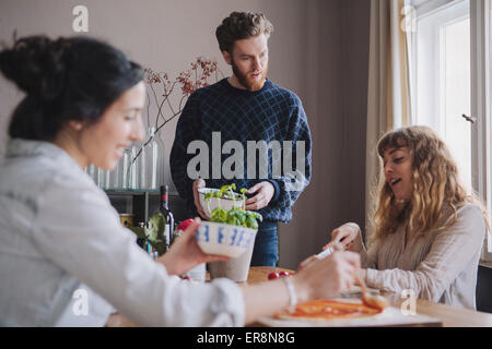 Young man with female friends making pizza at table Stock Photo