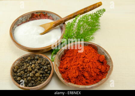 Plates filled with black pepper, paprika and salt and a green herb on a table Stock Photo
