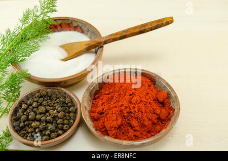 Plates filled with black pepper, paprika and salt and a green herb on a table Stock Photo